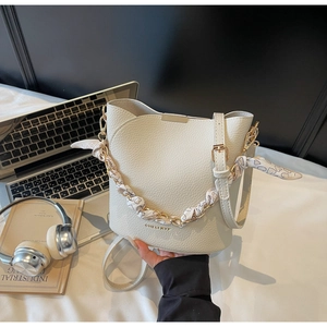 Détail du sac seau en cuir grainé blanc avec foulard en soie enroulé sur la chaîne dorée