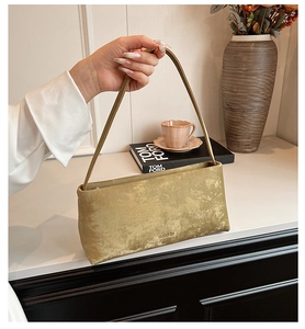 Close-up of metallic gold baguette bag showing the vintage textured fabric and logo