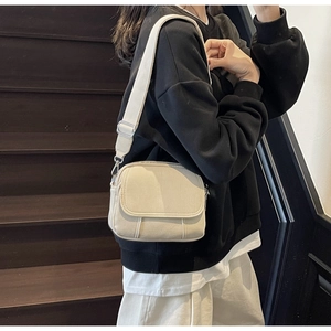 Model draagt een gebroken witte crossbodytas op een donkere houten trap detail