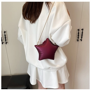 Macro shot of a wine red star-shaped crossbody bag with gold chain strap shown on a model
