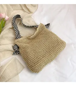 Dettaglio di borsa tote in paglia intrecciata con fiocco a righe bianche e nere sul manico