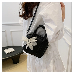 Detail of a chic black textured mini bag with white gauze floral charm and top handle