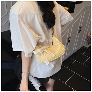 Model wearing a pale yellow patent leather crescent bag with lace bow and heart pearl