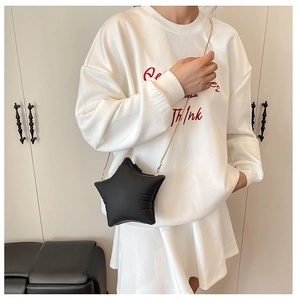 Detail view of black star-shaped crossbody bag with gold chain strap on white outfit