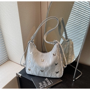 Detail of silver-grey textured shoulder bag with metallic butterfly accents and adjustable strap