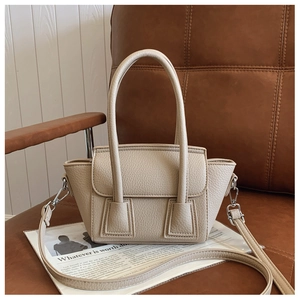 Detail view of beige lychee texture leather handbag with trapezoid shape on leather chair