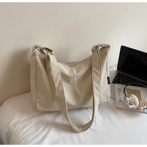 Close-up of beige canvas dumpling bag on desk with laptop and art book decor
