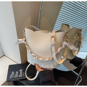 Détail du sac seau en cuir crème avec logo doré, anse chaîne et foulard en soie à cœurs