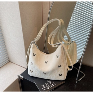 Detail of cream half-moon bag featuring metallic butterfly studs and pleated texture