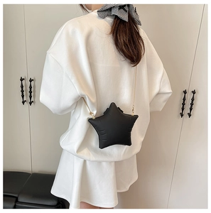 Star-shaped matte black crossbody bag with a delicate gold chain strap on white outfit