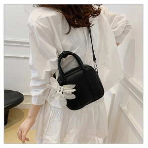 Detail of black pebbled leather crossbody bag featuring a 3D white mesh floral charm