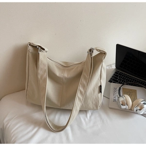 Beige canvas dumpling bag with adjustable wide strap shown in a modern lifestyle setting