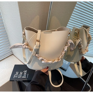 Détail du sac seau crème avec texture litchi et chaîne en métal ornée d'un foulard