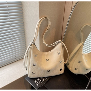Detail of off-white PU leather shoulder bag with metallic butterfly accents and sleek strap