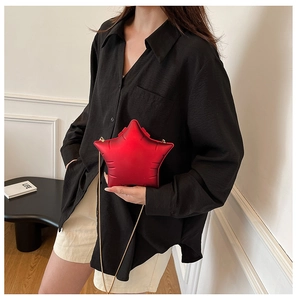 Detail of red star-shaped crossbody bag with gold chain strap on model's black shirt