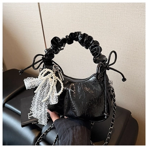 Détail d'un sac demi-lune en cuir verni noir avec nœud en dentelle et perles