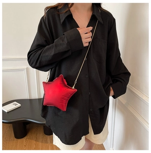 Detail of red star-shaped crossbody bag with gold chain strap on a black shirt backdrop