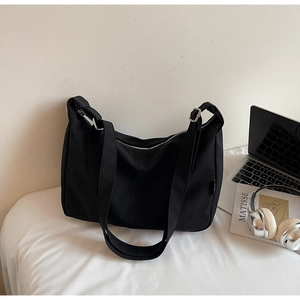 Minimalist black nylon tote bag shown with a laptop and book in a lifestyle setting