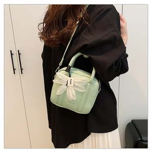 Detail of light green pebbled leather Boston bag with white silk flower charm accessory