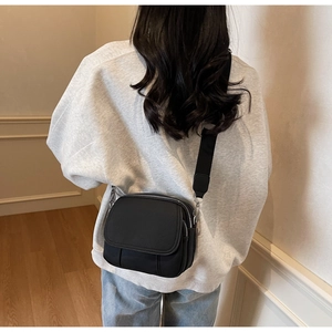 Detail van een zwarte crossbodytas met meerdere vakken en een brede stoffen riem