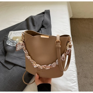 Détail du sac seau en cuir marron avec chaîne en foulard de soie et logo doré