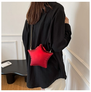 Close-up of star-shaped red crossbody chain bag with golden strap worn by model