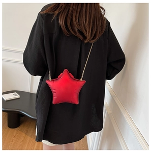 Detail of a red star-shaped crossbody bag with a gold chain strap on a black outfit