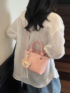 Pink pleated leather bucket bag with bear pendant shown on a model on wooden stairs
