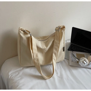 Detail of off-white canvas hobo bag with adjustable strap and zipper on white bedding