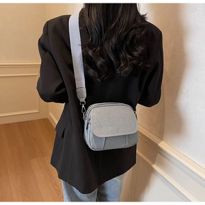 Detail van lichtgrijze canvas crossbodytas met brede geweven riem en rits
