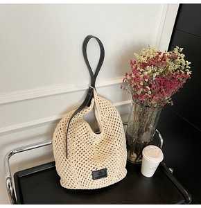Close-up of beige crochet shoulder bag with hollow knit pattern and black leather strap