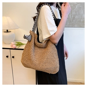 Dettaglio borsa tote in paglia intrecciata con tracolla a righe bianche e nere su modella