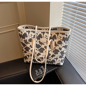 Close-up of a large cow print canvas tote bag with leather logo patch on a black chair