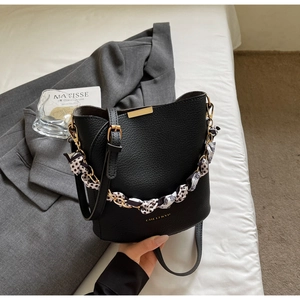 Detail of black lychee leather bucket bag with silk scarf handle and golden logo