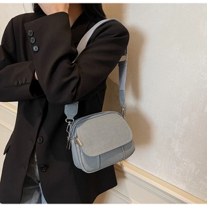 Detailweergave van lichtblauwe denim crossbodytas met brede riem en zilverkleurige gesp