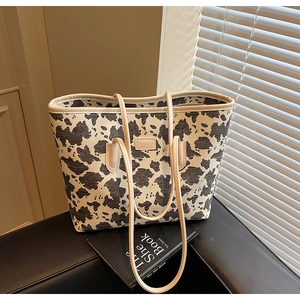 Close-up of a high-capacity cow print tote bag with creamy handles and leather logo