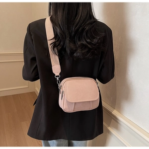 Detail van roze PU-leren crossbodytas met brede stoffen schouderband en zilveren hardware
