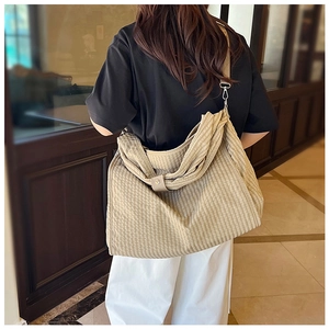 Detail of light brown checkered canvas tote bag showing wide strap and metal hardware