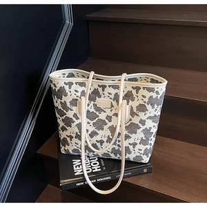 Close-up of cow print canvas tote bag with faux leather straps on wooden background