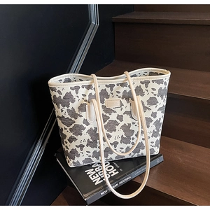 Close-up of a large canvas tote bag with black cow print and leather brand tag