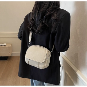 Detail van een crème canvas crossbodytas met meerdere ritsvakken en een brede stoffen riem