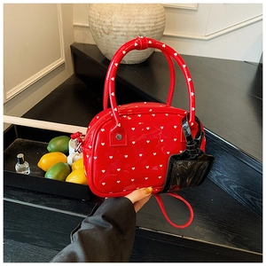 Detail of red patent leather bowling bag with heart print held by a model on dark stairs