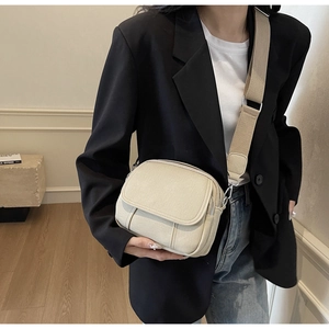 Detail van de crème crossbodytas met brede riem bij een model met een zwarte blazer