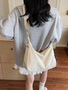 Minimalist cream canvas hobo bag with wide adjustable strap worn as a crossbody