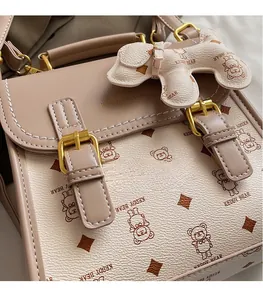 Close-up of beige lychee leather bag with cartoon bear prints and golden metal buckles