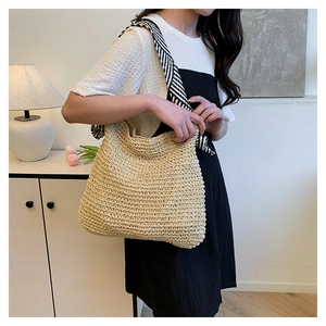 Dettaglio della borsa tote in paglia intrecciata a mano con tracolla moderna a righe bianche