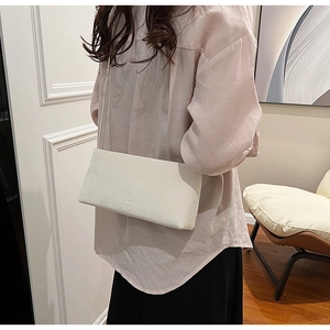 Detail of a minimalist white leather crossbody bag with subtle embossed logo on model