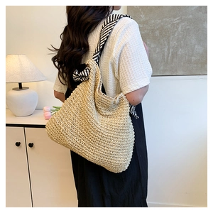 Dettaglio di una borsa tote in paglia intrecciata beige con tracolle a righe bianche e nere
