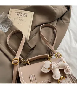 Detail of beige crossbody bag with teddy bear charm and adjustable leather strap