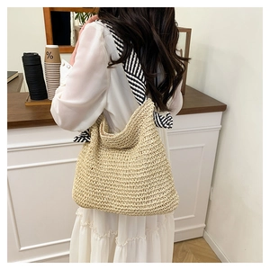 Dettaglio della borsa tote in paglia beige con tracolla a righe bianche e nere